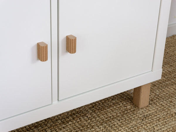 White ikea kallax cabinet with wooden knobs on a textured floor