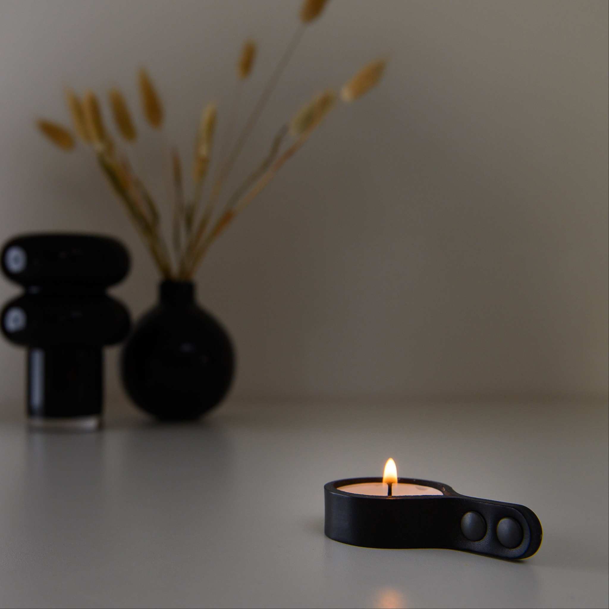 Minimalist leather tealight candle holder with rounded ends and lit candle on table