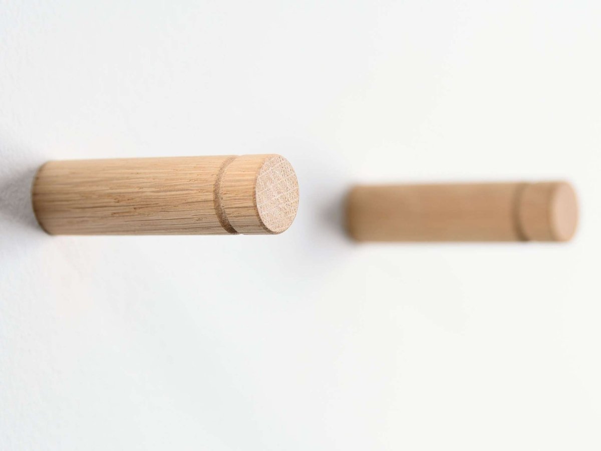 a pair of coat hooks from unfinished oak wood ona  white wall