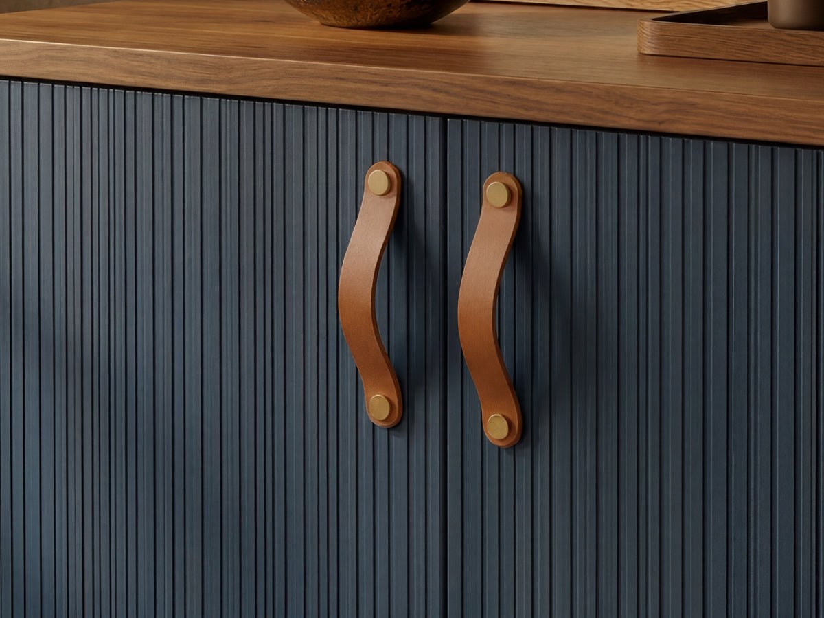Nahaufnahme eines Schranks mit dunkelblauen Türen mit vertikalen Lamellen und geschwungenen, hellbraunen Ledergriffen, gekrönt von einer Arbeitsplatte aus Holz.