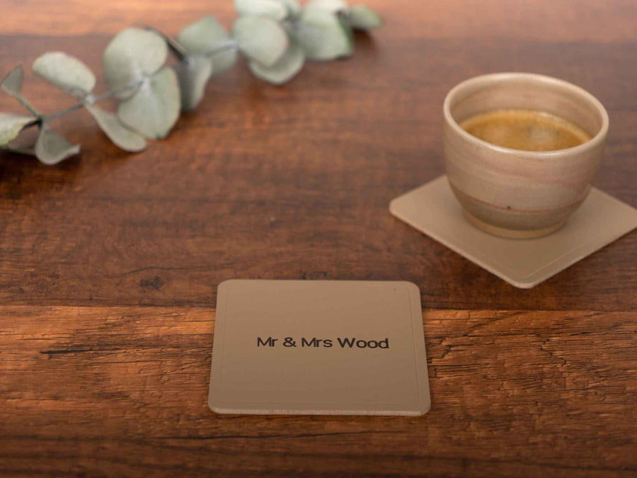 Square personalized leather coaster with Mr & Mrs Wood engraving on wood table next to coffee cup